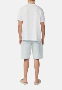 Witte katoenen t-shirt, lichtblauwe denim shorts en beige slippers. Het t-shirt heeft een ronde hals; de shorts hebben achterzakken en hebben een relaxte pasvorm.