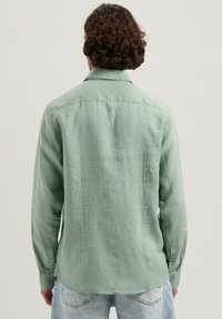 Camisa de manga larga verde claro hecha de una tela texturizada, con cuello y puños de botón, un dobladillo curvado y un detalle en la yugo trasero.