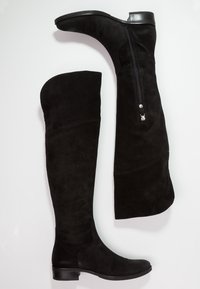 Botas negras de ante por encima de la rodilla, con cremallera lateral y puntera ligeramente redondeada, y un tacón bajo y apilado.