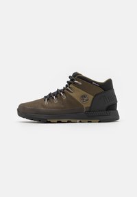Wysokie buty turystyczne w oliwkowym zielonym kolorze z czarną siateczką, z metalowymi oczkami, gumową podeszwą oraz logo Timberland po boku. Zaprojektowane z myślą o trwałości.