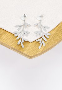 Orecchini in argento con un design a foglia, caratterizzati da rami intagliati e un supporto a perno circolare, esposti su una superficie texturizzata.