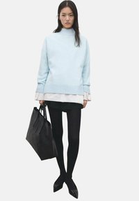 Svetlo modra prevelika majica z visokim ovratnikom, oblečena preko bele srajce. Črni kratki hlače, legice in črne špičaste čevlje. Črna torba za na rame.