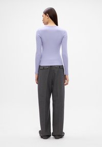 Lila Langarmtop mit taillierter Passform, kombiniert mit hoch taillierten grauen Nadelstreifen-Hosen mit zwei Gesäßtaschen und geradem Bein.