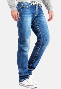 Spijkerbroeken in een middelblauwe wassing, met een aansluitend ontwerp, contrasterende witte stiksels en een ritsgulp. Gecombineerd met witte sneakers.