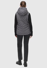 Houndstooth raksta vests ar augstu apkakli, melniem piedurknēm un pieguļošu siluetu, apvienots ar melnām džinsām un masīvām melnām zābakiem.