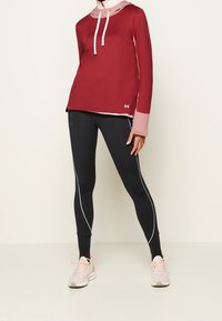 Červená sportovní mikina s růžovou vnitřní vrstvou, bílými stahovacími šňůrkami a otvory na palce, spojená s černými legínami s bílými postranními pruhy.