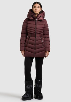Giacca puffa bordeaux con vita svasata e colletto alto, caratterizzata da linee trapuntate verticali e tasche con cerniera. Abbinata a stivali invernali neri.