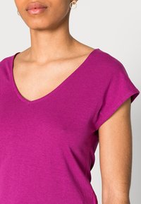 Fuchsia t-shirt med V-hals och korta ärmar, tillverkad av mjuk bomullstextil. Har en figurnära passform och minimala sömdetaljer.