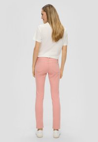 Jeans rosa claro con corte ajustado, que cuentan con bolsillos traseros y cierre de botón. Combinados con una camiseta blanca y zapatillas blancas.