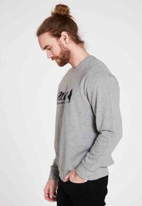 Grå sweatshirt lavet af blødt stof, med lange ærmer, rund halsudskæring og et trykt design i mørkeblå på brystet.