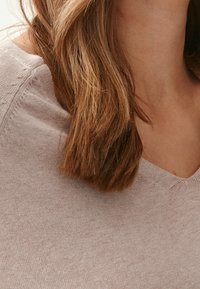 Jasnoróżowy sweter dziergany o dekolcie w serek i miękkiej fakturze, zbliżenie na linię szyi i obszar kołnierza.