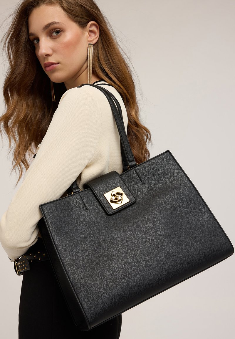 Borsa a mano in pelle nera con un design strutturato, caratterizzata da una chiusura geometrica dorata e due manici robusti. Superficie texturizzata, forma rettangolare.