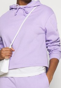 Ljust lila huvtröja med avslappnad passform, med snörning i halsen, ribbad mudd och lager av vit undertröja.