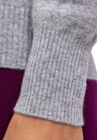 Grau gestrickter Pulloverbund mit gerippter Textur, Nahaufnahme des Stoffdetails. Der Hintergrund zeigt ein tiefes lila Textil.