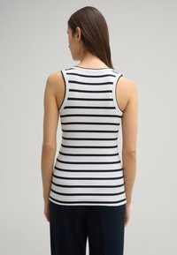 Gestreepte mouwloze top in wit en marineblauw, met een geribbelde textuur. Het heeft een ronde halslijn en sluit nauw aan op het lichaam.
