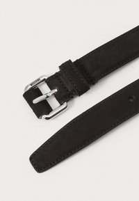 Cinturón de ante negro con hebilla de metal plateado. Presenta detalles de costura y agujeros de ajuste a lo largo de la correa. Nombre de la marca visible en la hebilla.