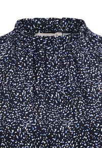 Dunkelblaue Bluse mit gerafftem Ausschnitt, verziert mit einem Muster aus verstreuten hellblauen und weißen Punkten auf einem strukturierten Stoff.