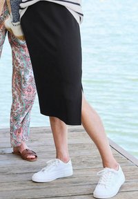 Schwarzer Midi-Rock mit Seitenschlitz, kombiniert mit weißen Mesh-Sneakern. Die Textur ist glatt mit einer figurbetonten Passform, geeignet für die Freizeit.