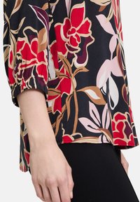 Bloes met bloemenprint op een zwarte achtergrond, levendige rode, roze en beige patronen, met elastische mouwen en een losse pasvorm.