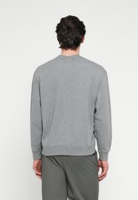 Sivá mikina s okrúhlym výstrihom, dlhými rukávmi a rebrovanými manžetami. Zadná strana má jednoduchý dizajn a mäkkú, textúrovanú tkaninu.