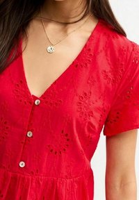 Czerwona sukienka z haftem w kwiaty, dekoltem w kształcie litery V, krótkimi rękawami i ozdobnymi guzikami z przodu. Lekka tkanina o miękkiej teksturze.