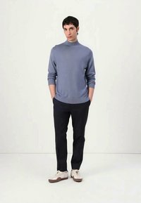 Sweater azul claro com gola alta, punhos canelados, combinado com calças escuras e ténis creme com solas castanhas. Design minimalista.