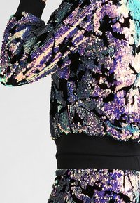 Veste noire à paillettes avec motifs floraux multicolores, poignets et ceinture côtelés. Texture douce avec paillettes scintillantes sur toute la surface.