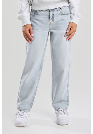 Jeans de mezclilla de tiro alto en azul claro, con un ajuste relajado, que presentan un diseño de cinco bolsillos y presillas para cinturón, combinados con zapatillas blancas.
