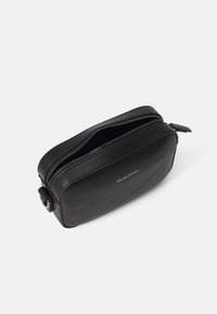 Trousse de maquillage en cuir noir de forme rectangulaire, avec fermeture éclair et logo en relief sur le devant. Texture lisse, design minimaliste.
