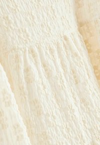 Tissu texturé couleur crème avec un motif froncé, présentant de petits motifs en relief. Doux, léger, adapté aux vêtements ou à l'ameublement.