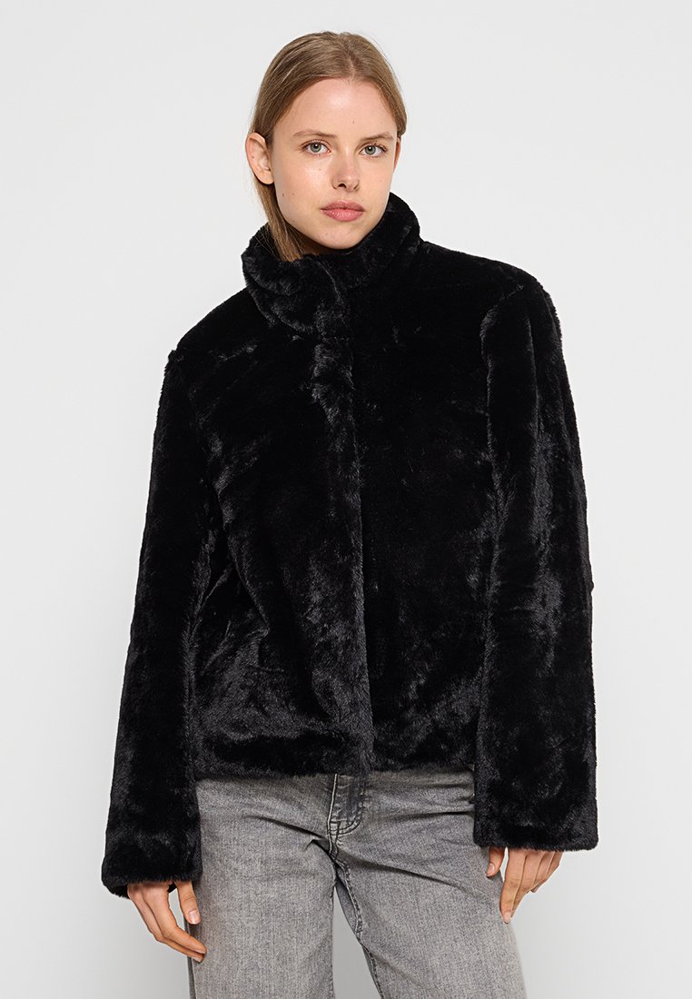 Schwarze Faux-Fur-Jacke mit Stehkragen, langen Ärmeln und boxy Schnitt. Glatte Textur, keine sichtbaren Beschläge oder Muster.
