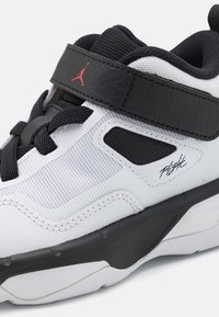 Sneaker bianca con accenti neri, materiali in rete e pelle, colletto imbottito, suola in gomma, con logo rosso e scritta stilizzata sul lato.