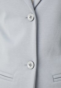 Lichtgrijze blazer van gestructureerde stof met een getailleerd ontwerp, voorzien van twee knopen, zijzakken en een zachte binnenvoering.