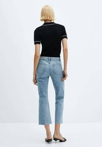 Camisa polo negra con ribetes blancos, combinada con jeans cortos azul claro con un dobladillo deshilachado y dos bolsillos traseros. Estilizada con tacones negros.
