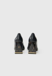 Pair of black leather heels with thick marbled block heels and gold trim viewed from the back on a plain gray background.