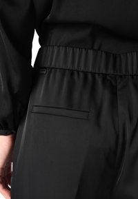 Pantaloni neri, simili a satin, con vita elastica, texture liscia e una tasca posteriore singola con apertura orizzontale.