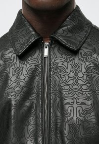 Μαύρο δερμάτινο μπουφάν με υφή που διαθέτει αφηρημένα σχέδια, κλασικό γιακά και εμπρόσθιο φερμουάρ.