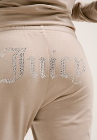 Beige fluwelen broek met rhinestone versieringen die "Juicy" op de achterkant spellen, met een zachte textuur en een aansluitend ontwerp.