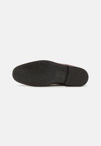 Semelle en cuir marron avec une semelle extérieure en caoutchouc noir texturé, présentant un motif de semelle pour une meilleure adhérence et un bord supérieur en cuir lisse.