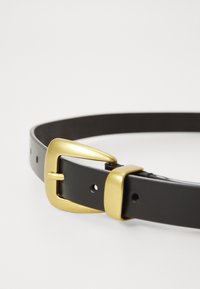 Ceinture en cuir noir avec une finition lisse. Dotée d'une boucle et d'un ergot en métal doré, avec plusieurs trous pour l'ajustement.