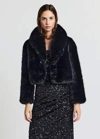 Schwarze Jacke aus Kunstpelz, kurz geschnitten, mit breitem Kragen und langen Ärmeln, weiche Textur, getragen über einem schwarzen, mit Pailletten besetzten Kleid. Glatte, glänzende Oberfläche.