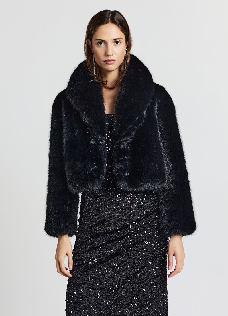 Schwarze Jacke aus Kunstpelz, kurz geschnitten, mit breitem Kragen und langen Ärmeln, weiche Textur, getragen über einem schwarzen, mit Pailletten besetzten Kleid. Glatte, glänzende Oberfläche.
