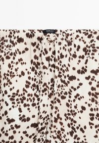 Světle béžová látka s hnědým leopardím vzorem, s elastickým pasem na šňůrku. Hladká textura, volný design, vhodné pro pohodlné nošení.