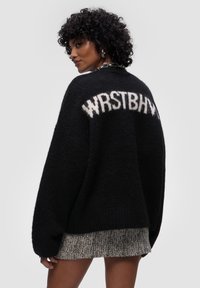 Czarny, oversize sweter wykonany z miękkiej dzianiny, z wyraźnym białym napisem "WRSTBHV" na plecach. Teksturowany, luźny krój.