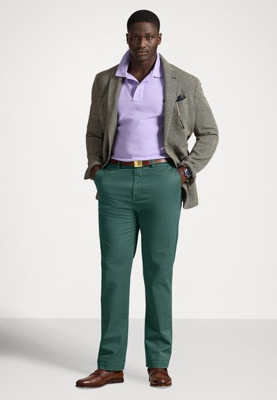 Ανδρικό σύνολο με δομημένο γκρι σακάκι, λιλά πόλο πουκάμισο, πράσινο παντελόνι, καφέ παπούτσια και χρυσή αγκράφα ζώνης.