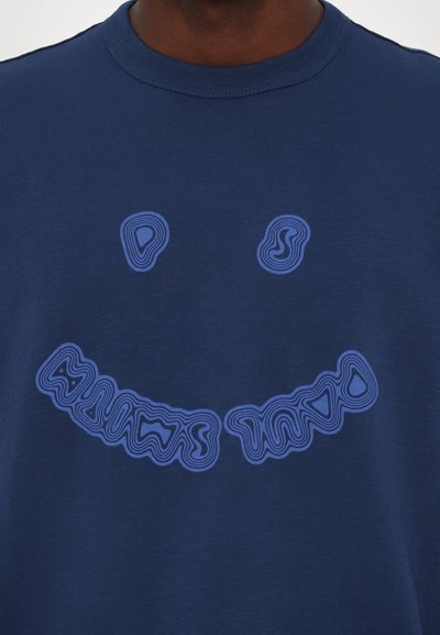 T-shirt en coton bleu marine avec un grand design de smiley bleu ondulé, comprenant des formes abstraites pour les yeux et la bouche.