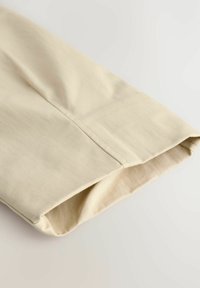Heled beige kangas, millel on sile tekstuur, lihtsa ja puhta disainiga, volditud varrukaga, millel on peene õmbluse detail.