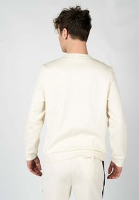 Sudadera color crema con mangas largas y cuello redondo. Textura suave, puños y cinturilla de canalé. Sin logotipos ni patrones visibles.