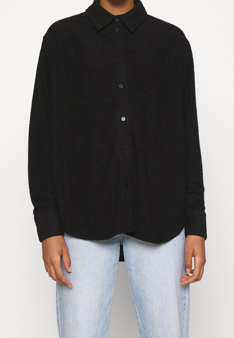 Sort skjorte med knapper i et blødt stof med krave, der har lange ærmer, en afslappet pasform og rundet nederkant. Kombinationen er med lyseblå jeans.