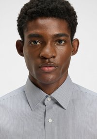 Knapp-up skjorta med ett litet blått och vitt vertikalt randigt mönster, med en klassisk krage och vita knappar, tillverkad av lättviktig tyg.